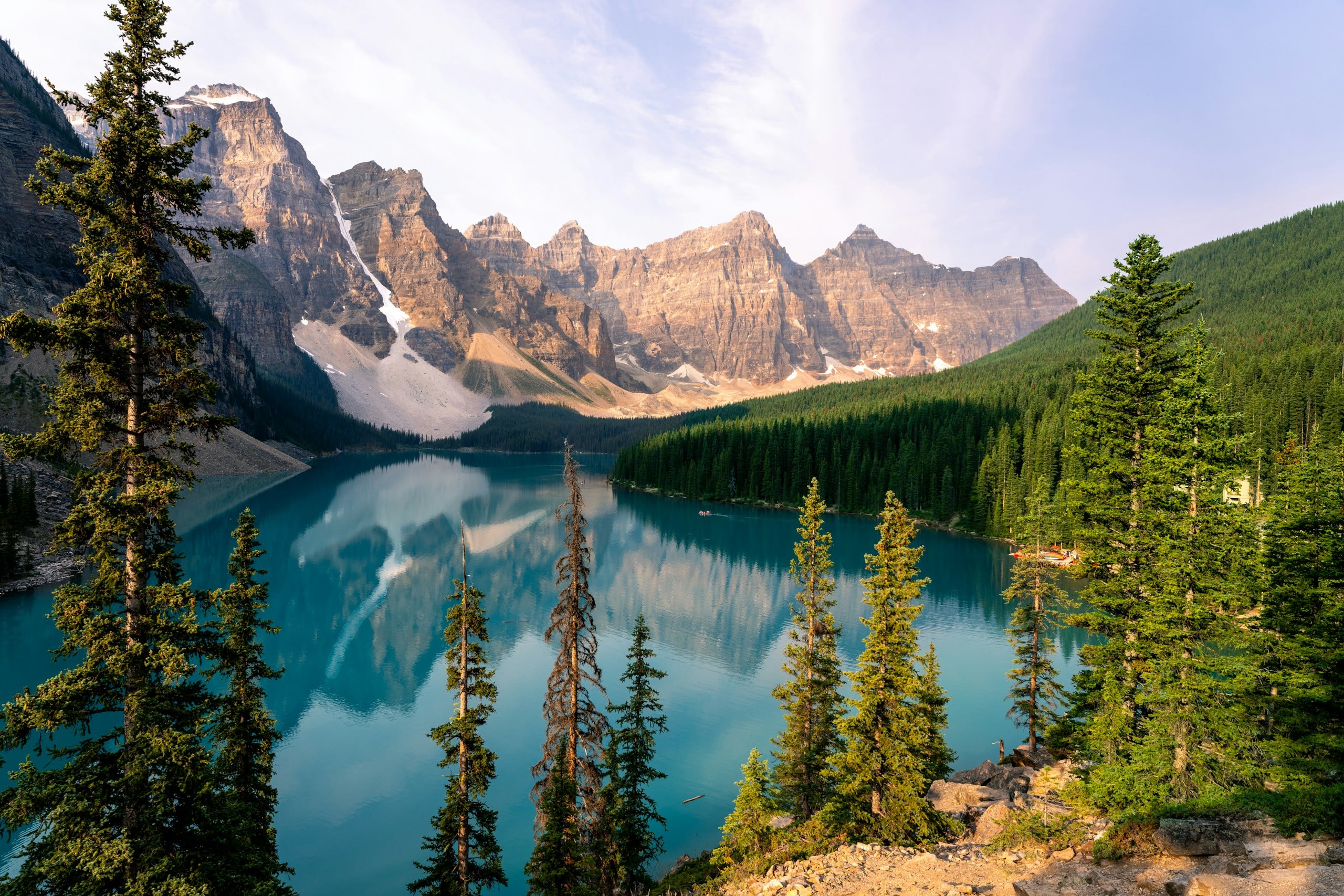 A lake surrounded by trees and mountains under a blue sky
