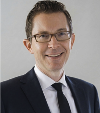 Andrew Bikichky smiling, wearing glasses, a dark suit and tie