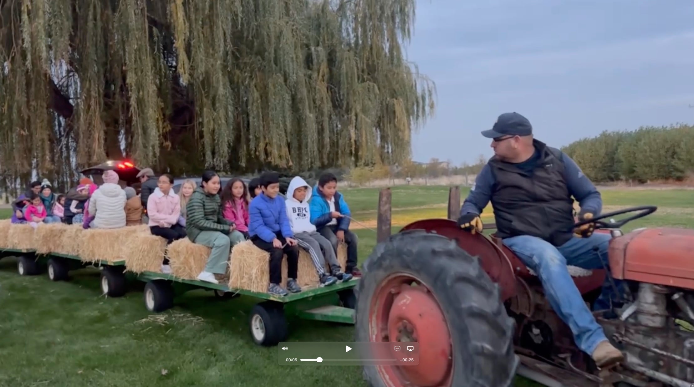 Children and adults riding on hay bales in a trailer pulled by a red tractor