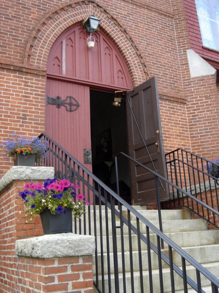 Open red front doors of Amesbury Seventh-day Adventist Church with flowers on the steps