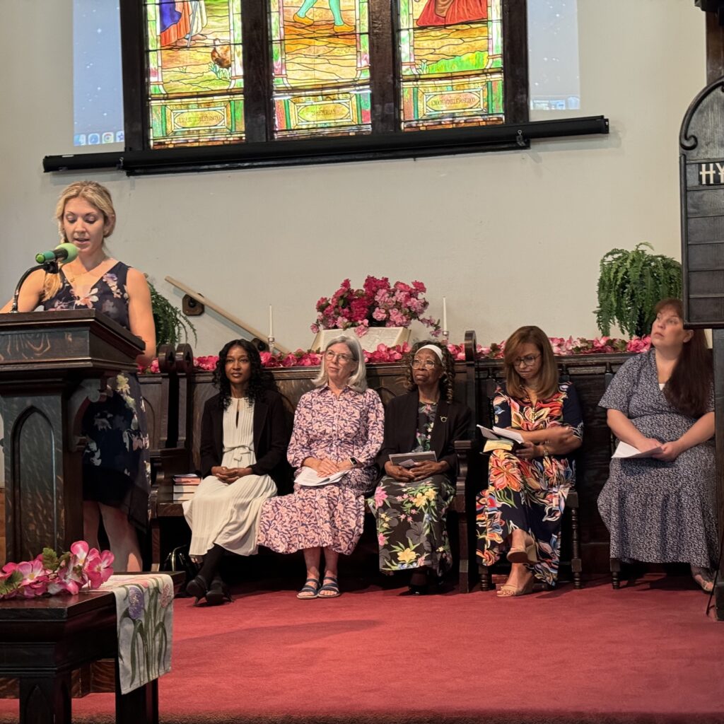 Women’s program on the platform in front of the stained glass window