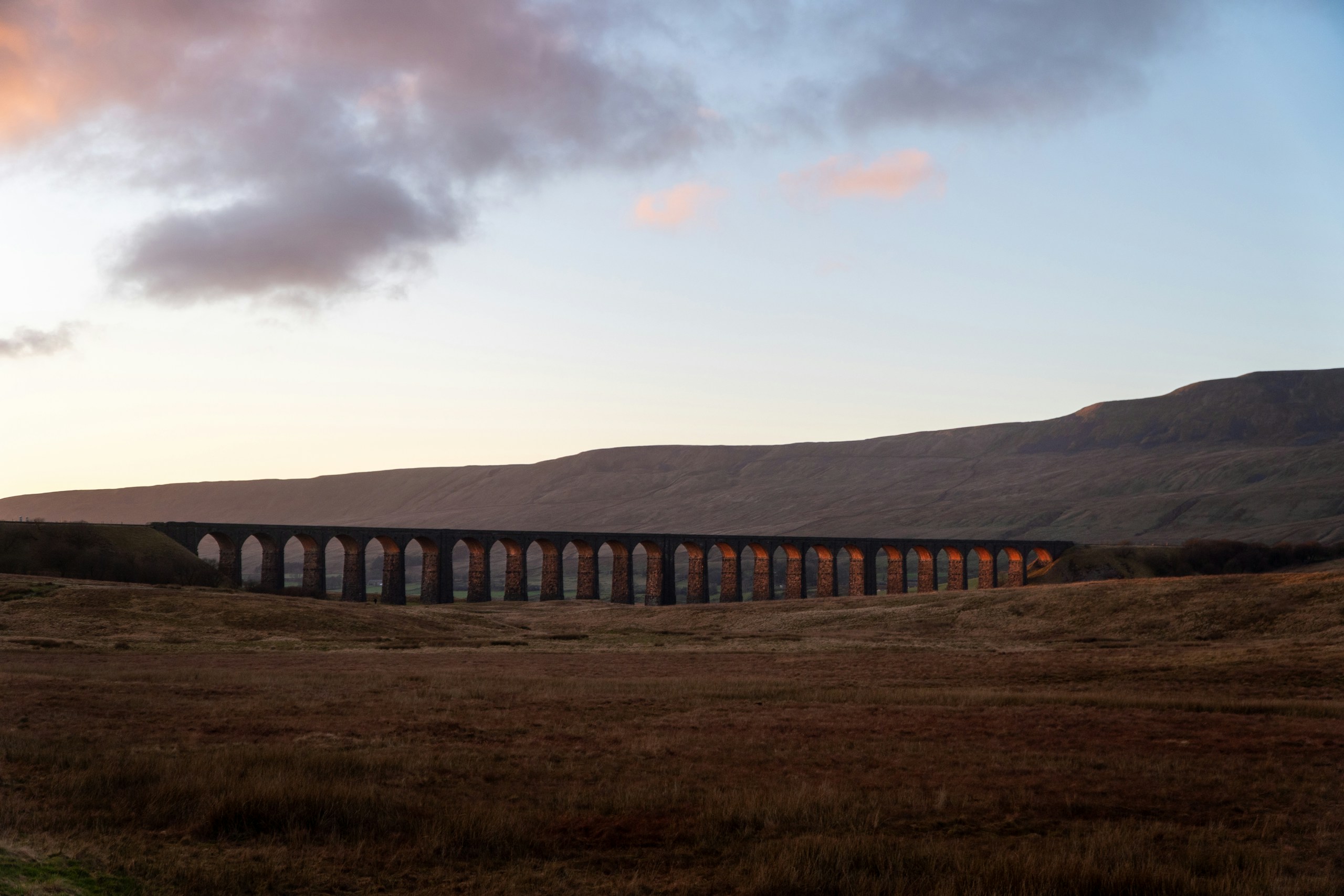 Stone railway viaduct in a moorland landscape at dusk.