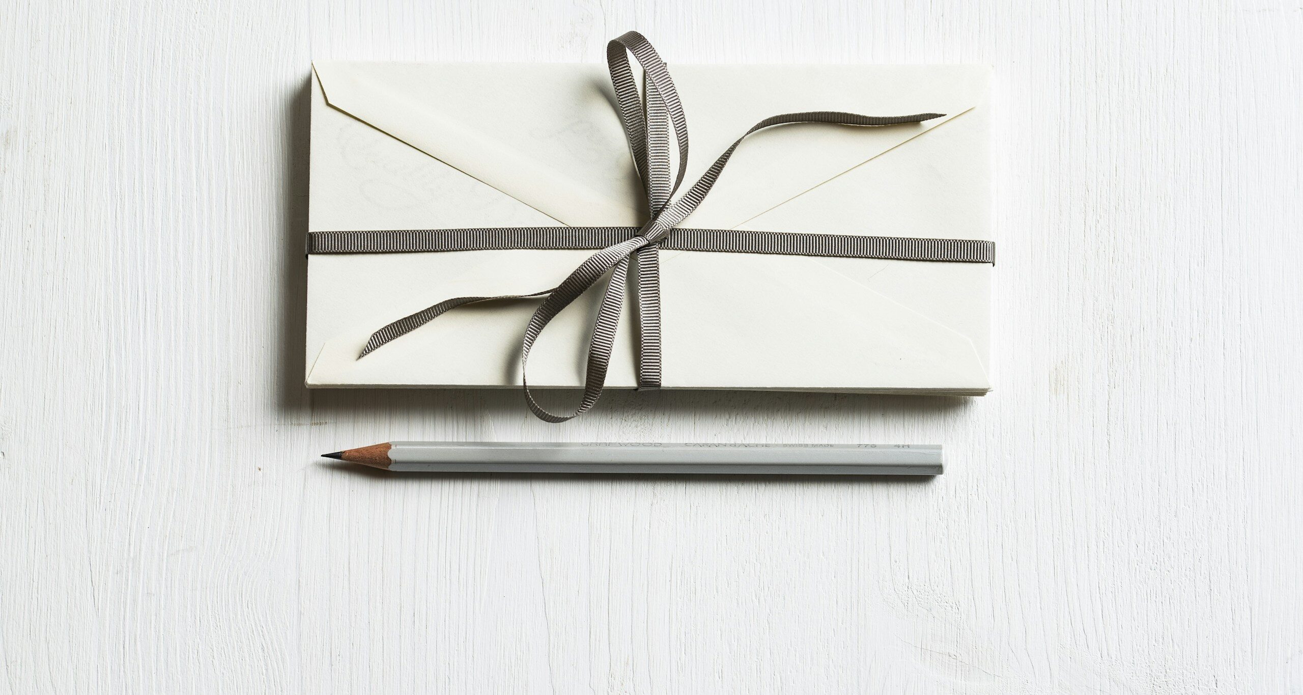 white envelop and gray pencil on white panel