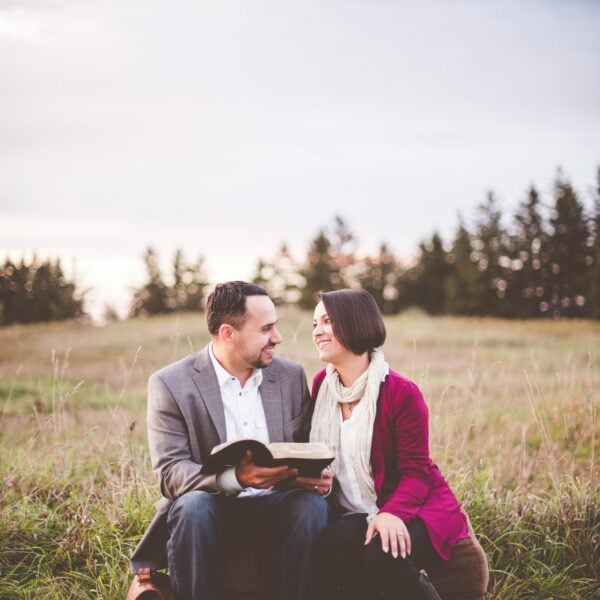 photo of man reading book to woman under grey cloudy sky