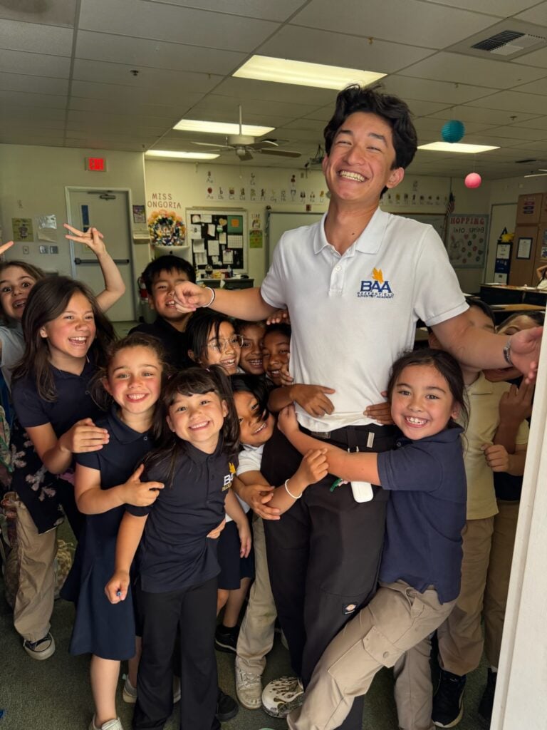 A BAA teacher smiling with a group of elementary students in a classroom