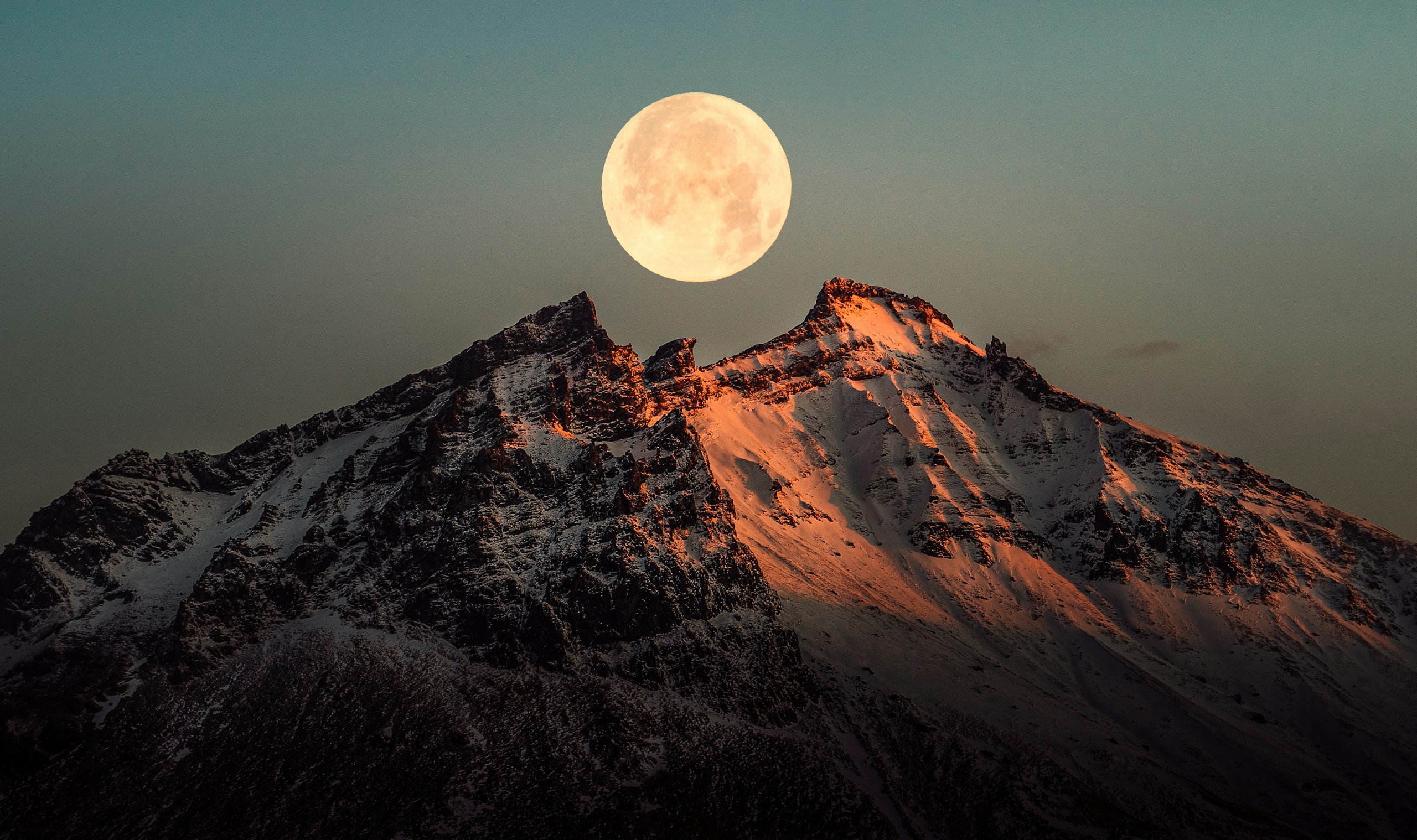 a full moon rising over a snowy mountain