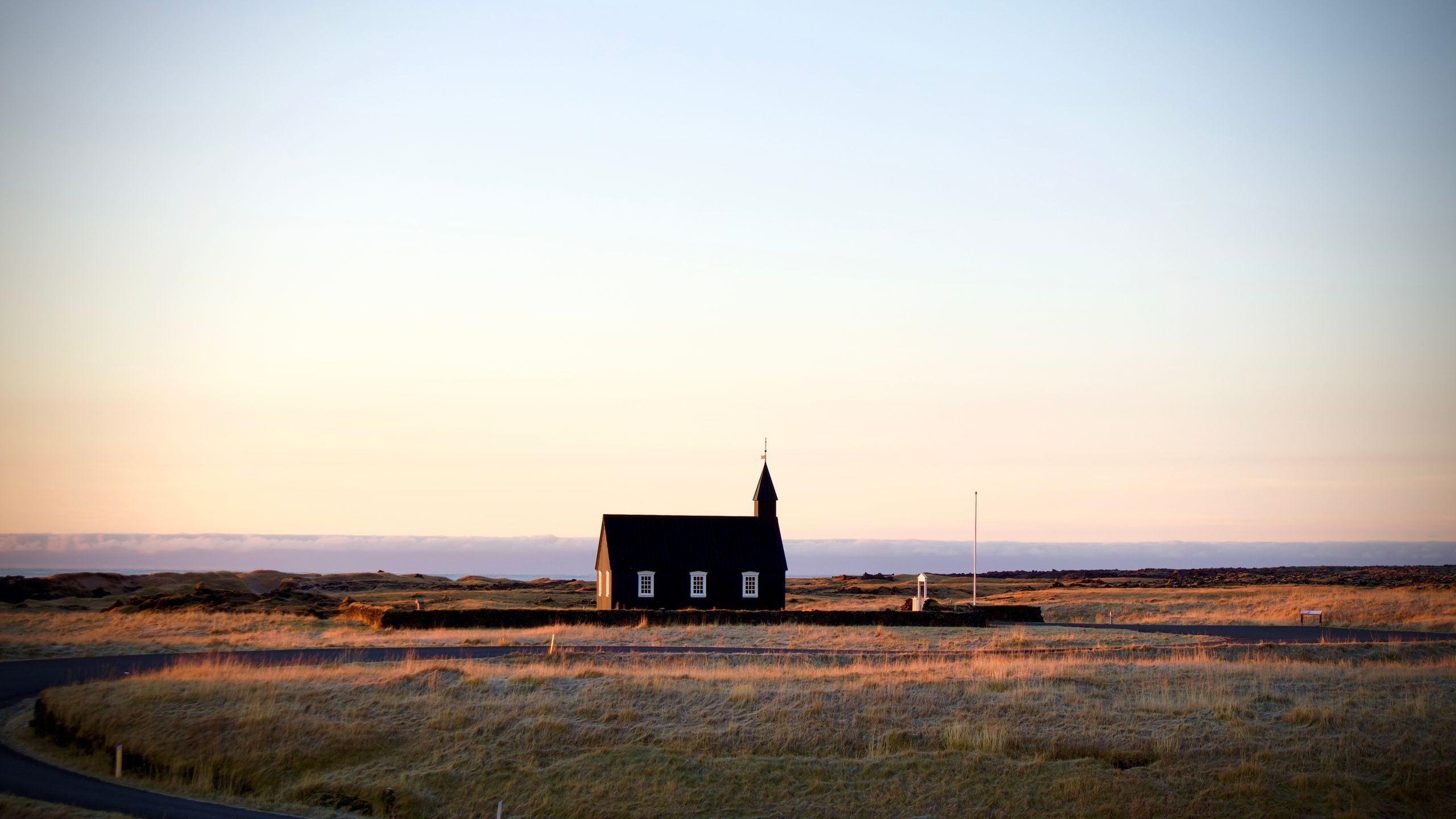 Black church in Iceland's countryside at sunset, showcasing rural serenity and unique architecture.