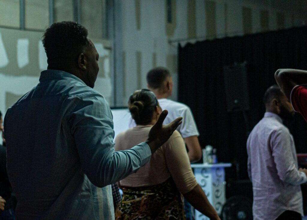 Back view of a group gathered in prayer at a modern indoor church setting with a casual ambiance.