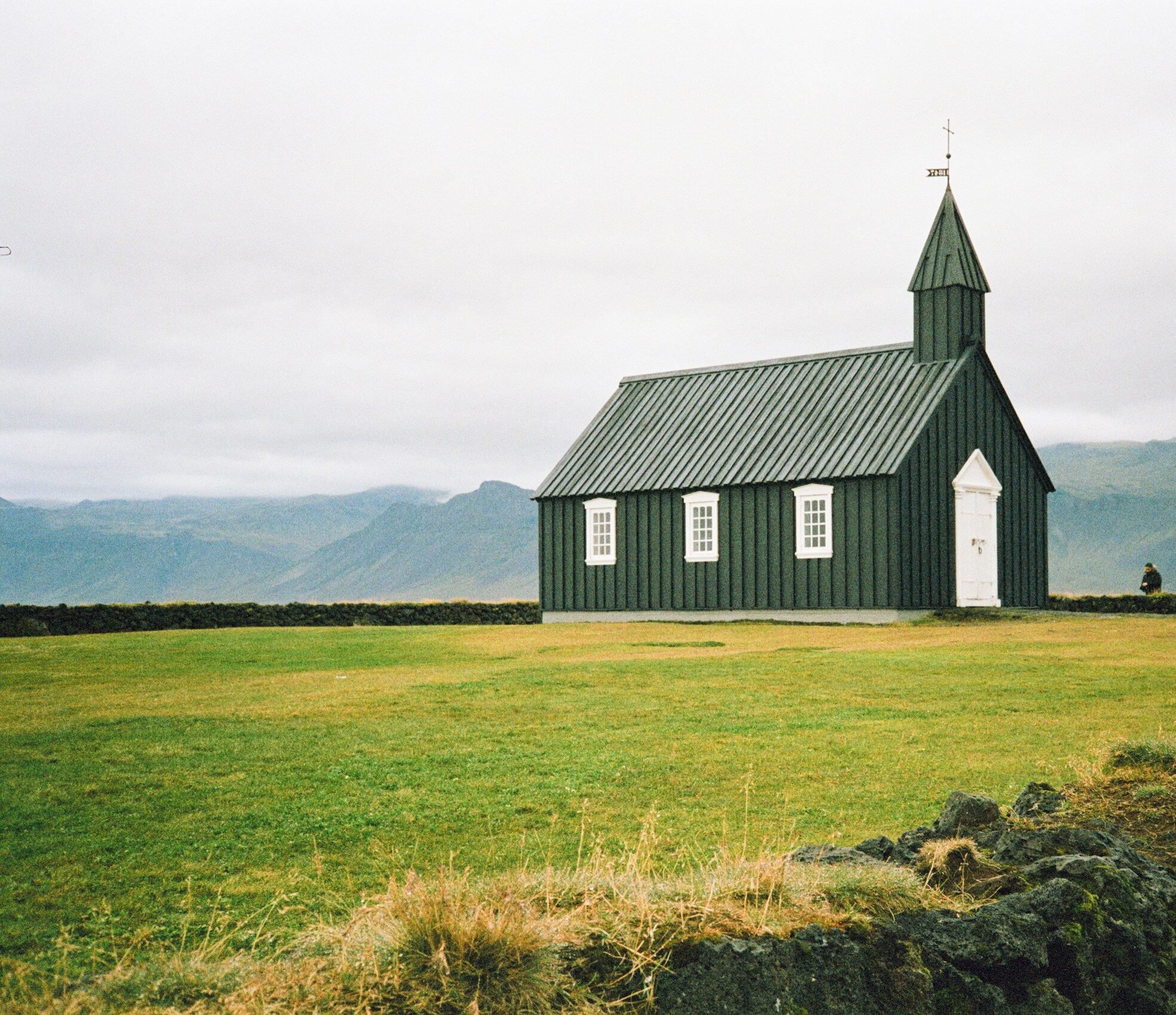 a green church with a steeple on a grassy hill