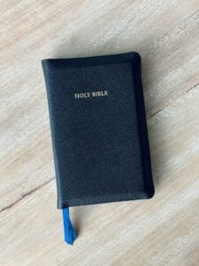 a black bible on a wooden table with a blue tassel