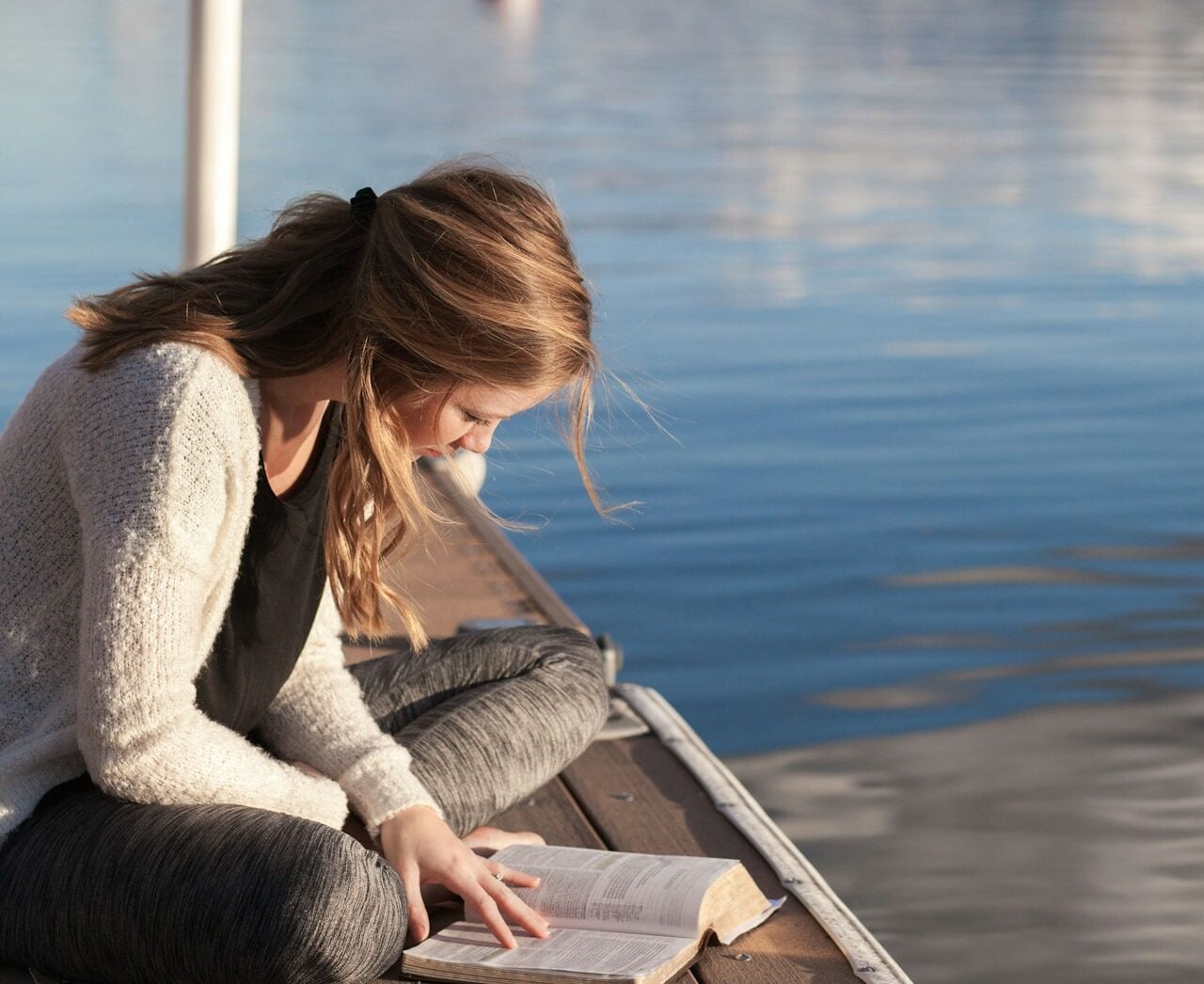 photo of woman reading book near body of water