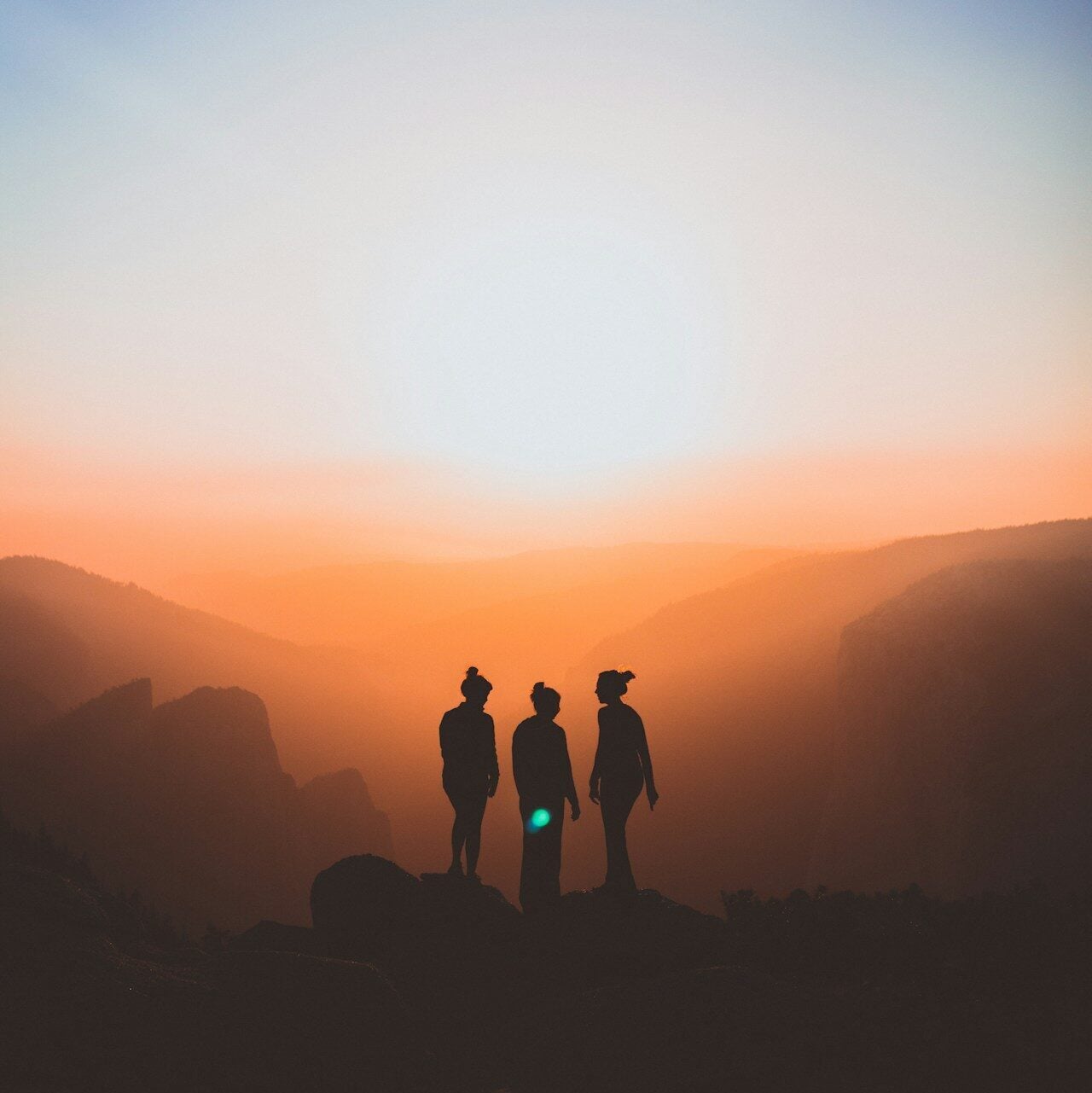 silhouette of three people up on mountain cliff