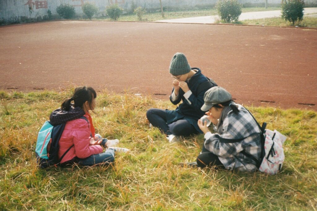 a group of people sitting on top of a grass covered field