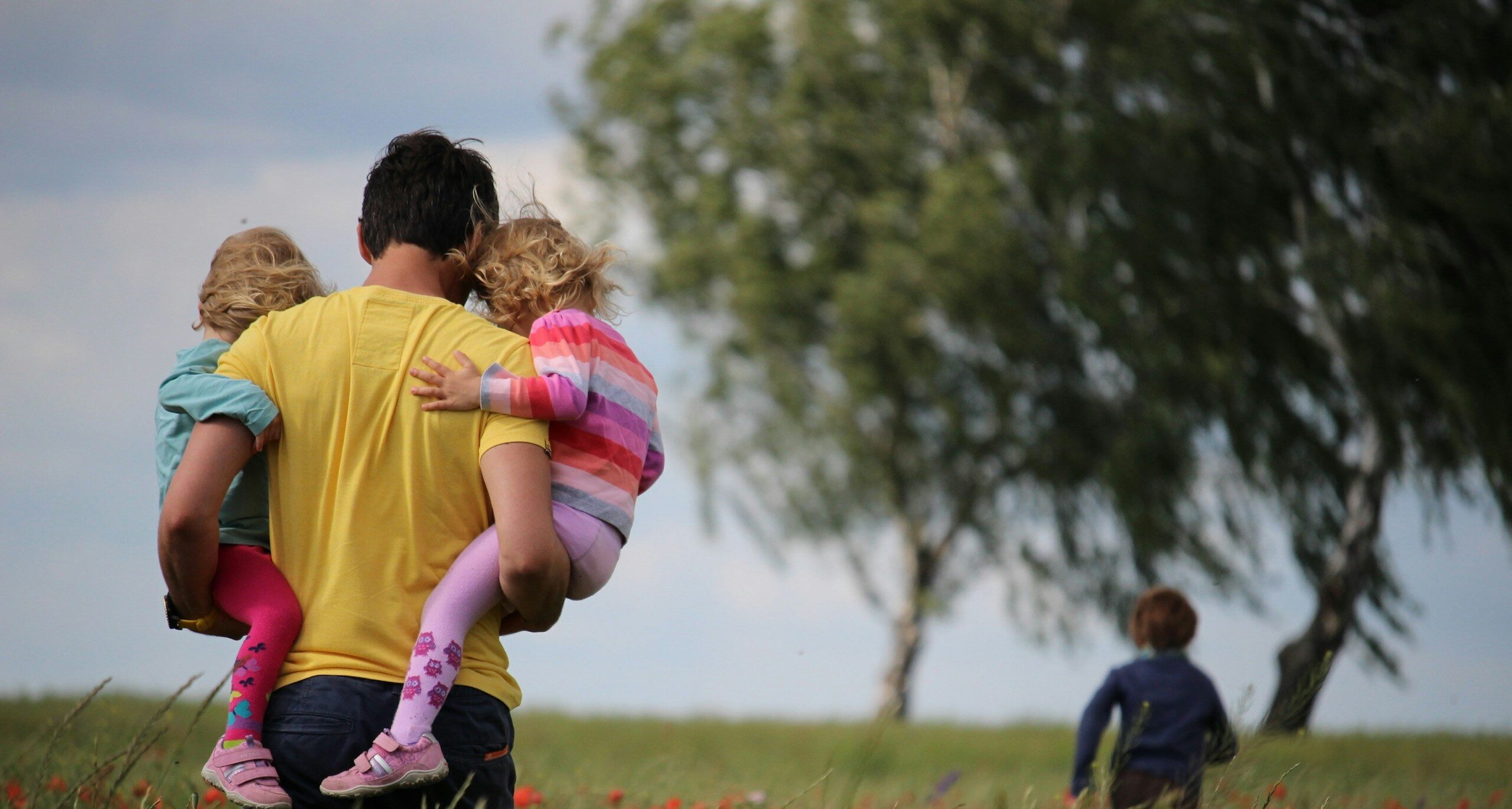man carrying to girls on field of red petaled flower