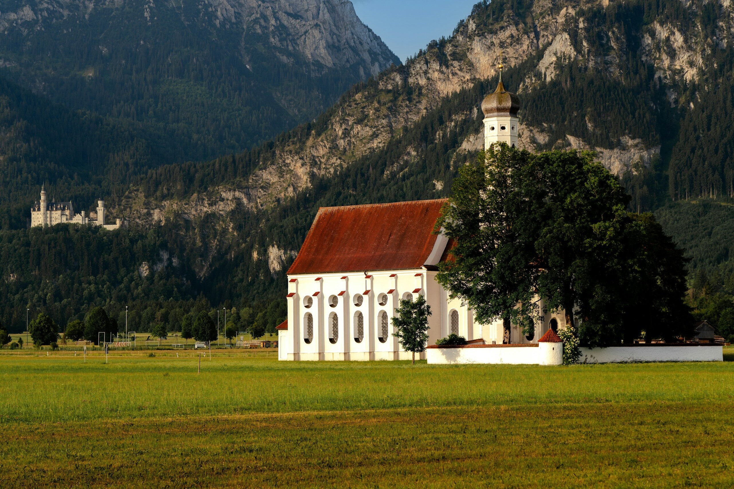 a church in the middle of a field with mountains in the background
