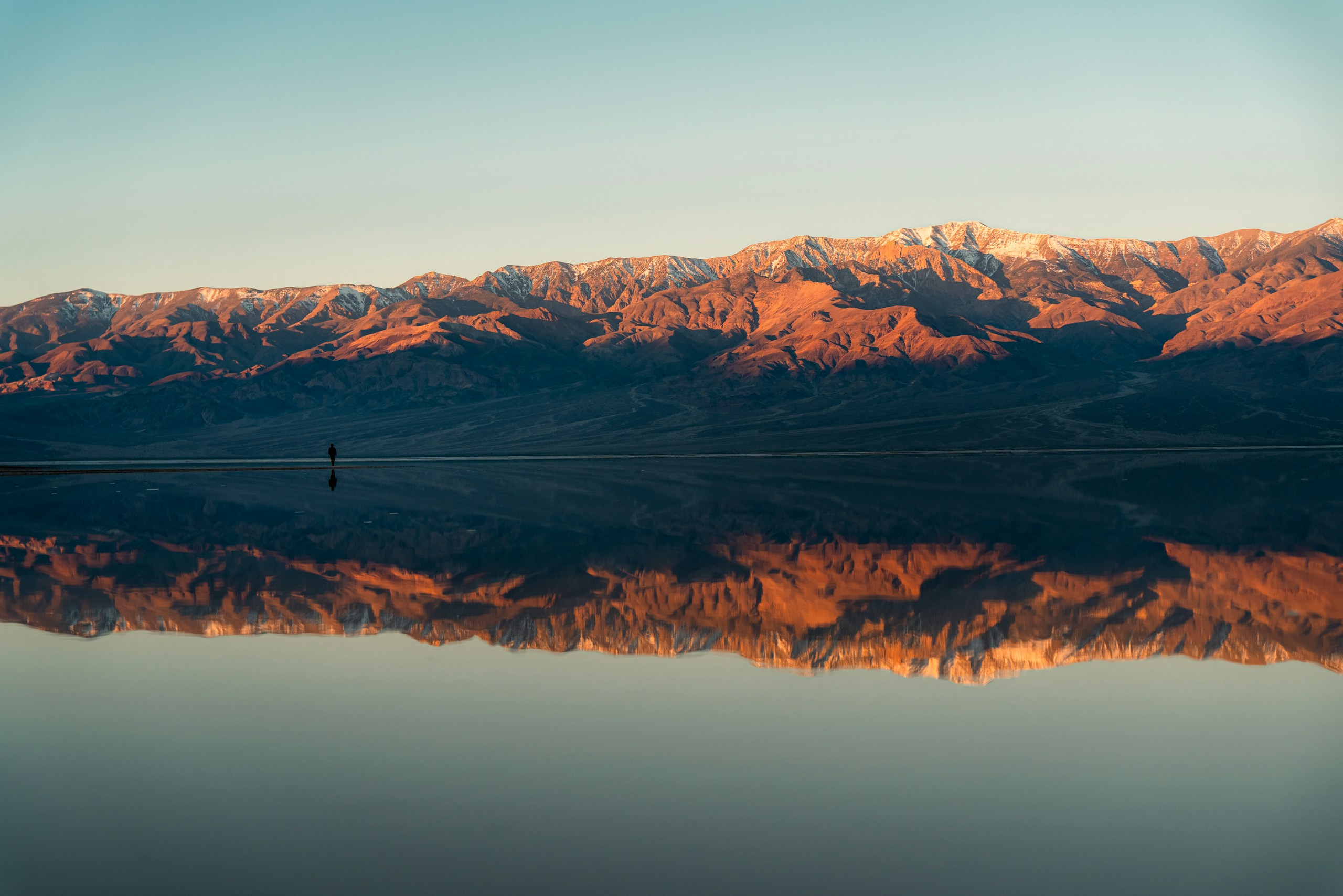 Snow-capped mountains reflecting in calm water at sunset