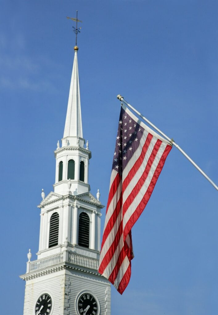 A church steeple and american flag stand tall.