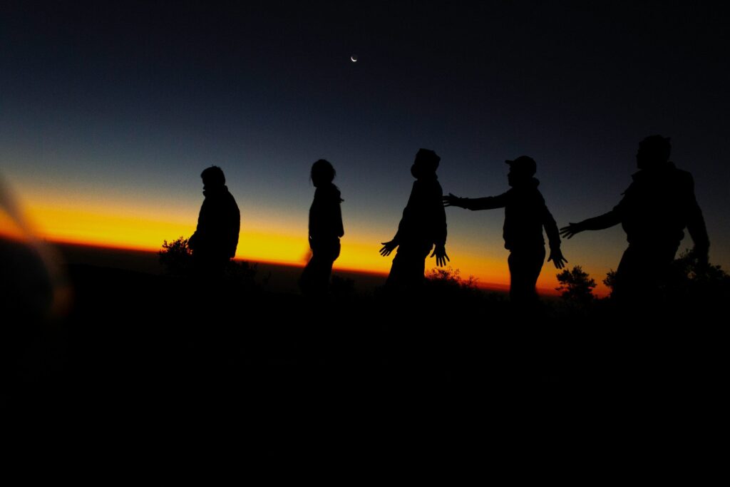 A group of people walking across a field at sunset