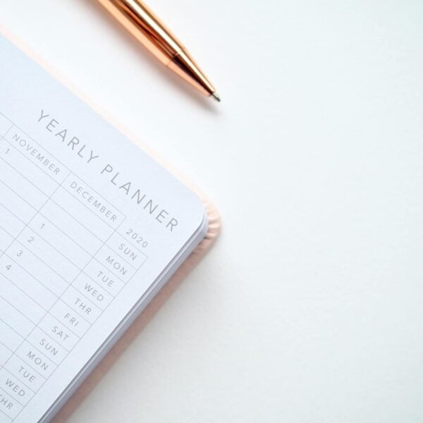 A stylish yearly planner open to a 2020 calendar page, accompanied by a golden pen on a clean white surface.