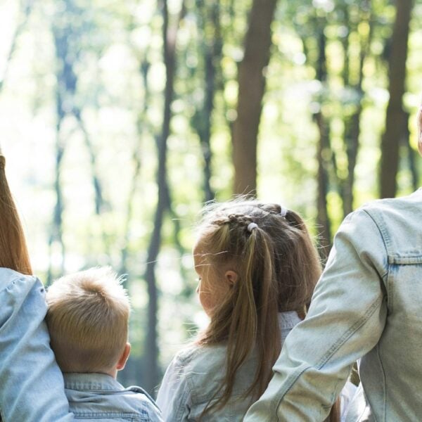 man and woman holding hands together with boy and girl looking at green trees during day