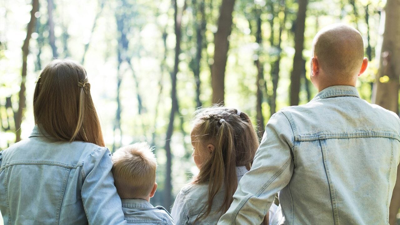 man and woman holding hands together with boy and girl looking at green trees during day