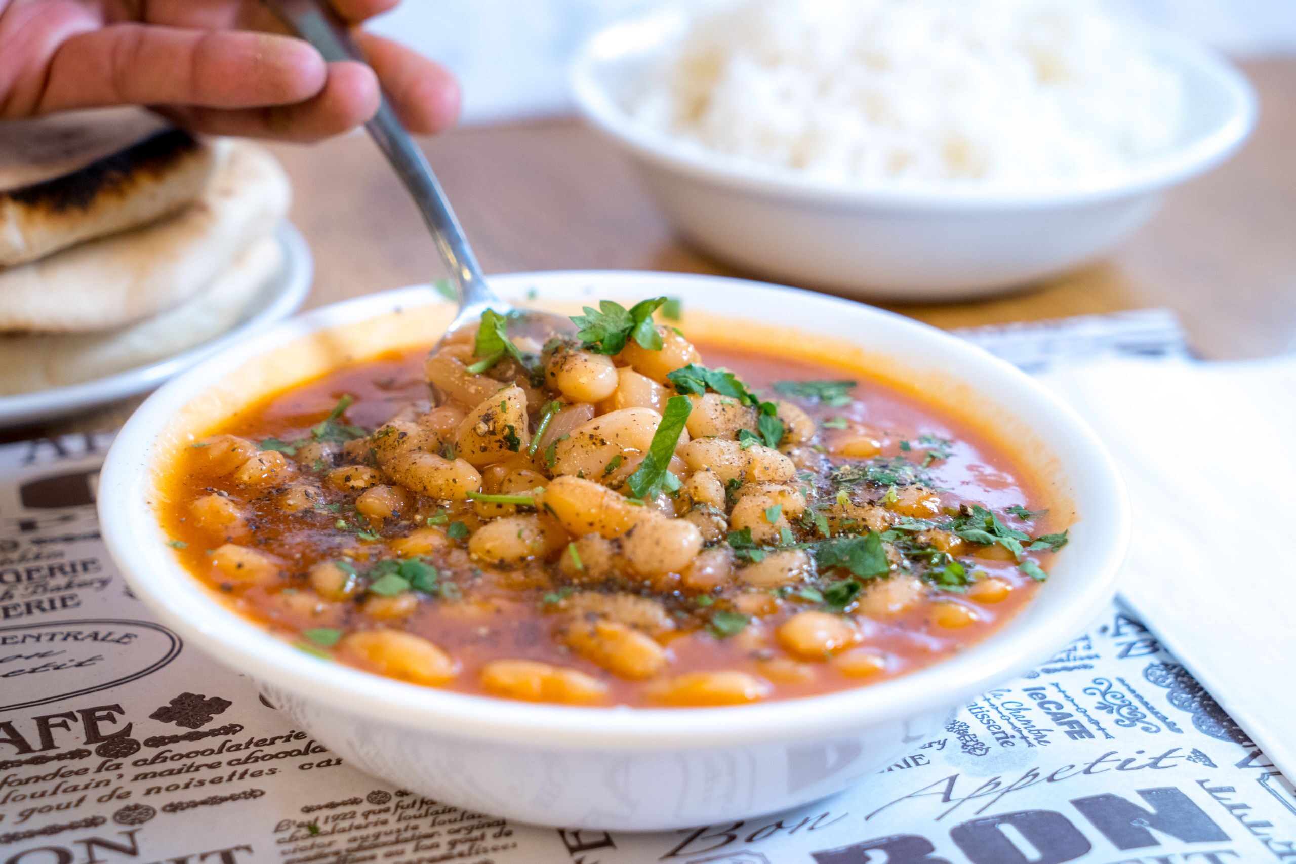 A bowl of hearty bean soup garnished with herbs, served with flatbread and rice.