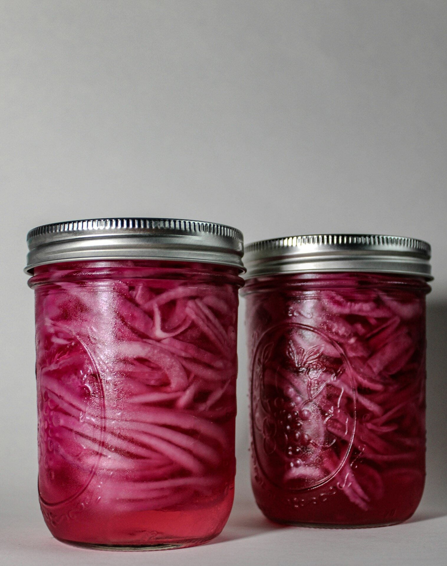 Two jars of vibrant pickled red onions.