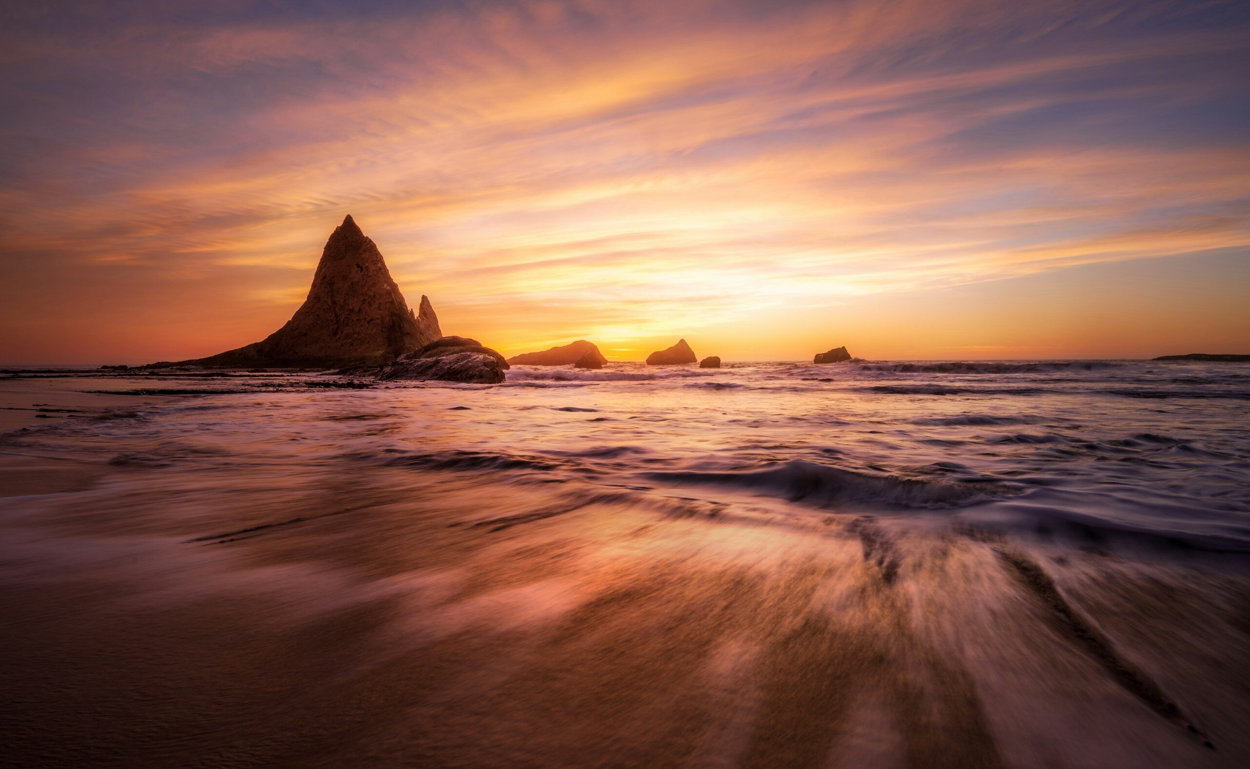 Dramatic sunset over a rocky coastline with ocean waves.