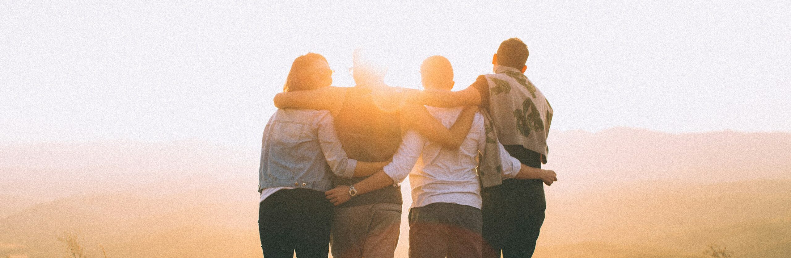 four person hands wrap around shoulders while looking at sunset