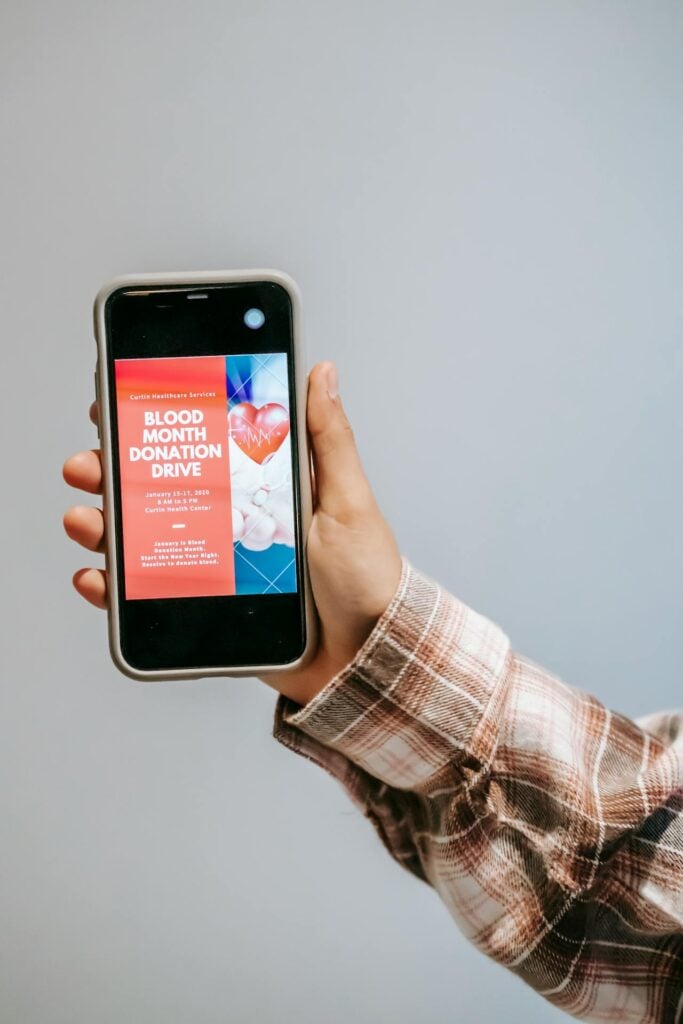 Close-up of a hand holding a smartphone with a blood donation drive display.