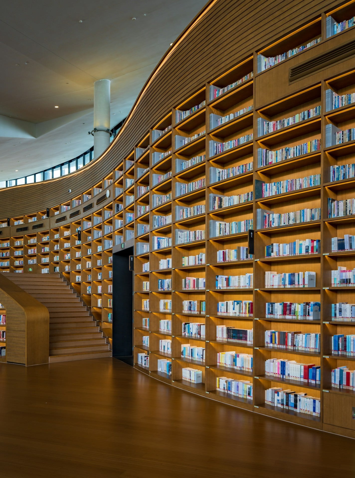Curving library shelves filled with books and a staircase.