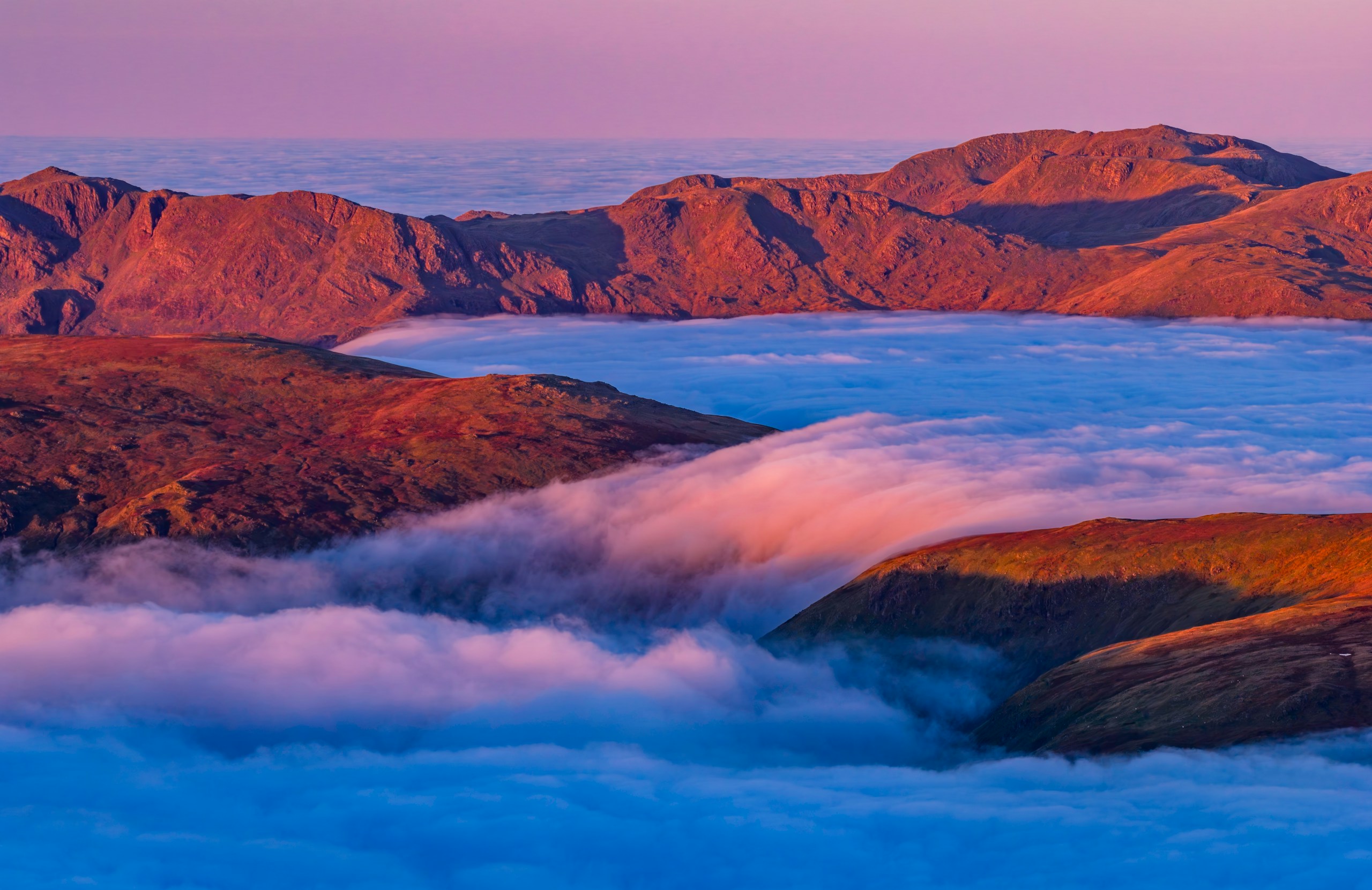 Mountain peaks emerge from a sea of clouds at sunrise.