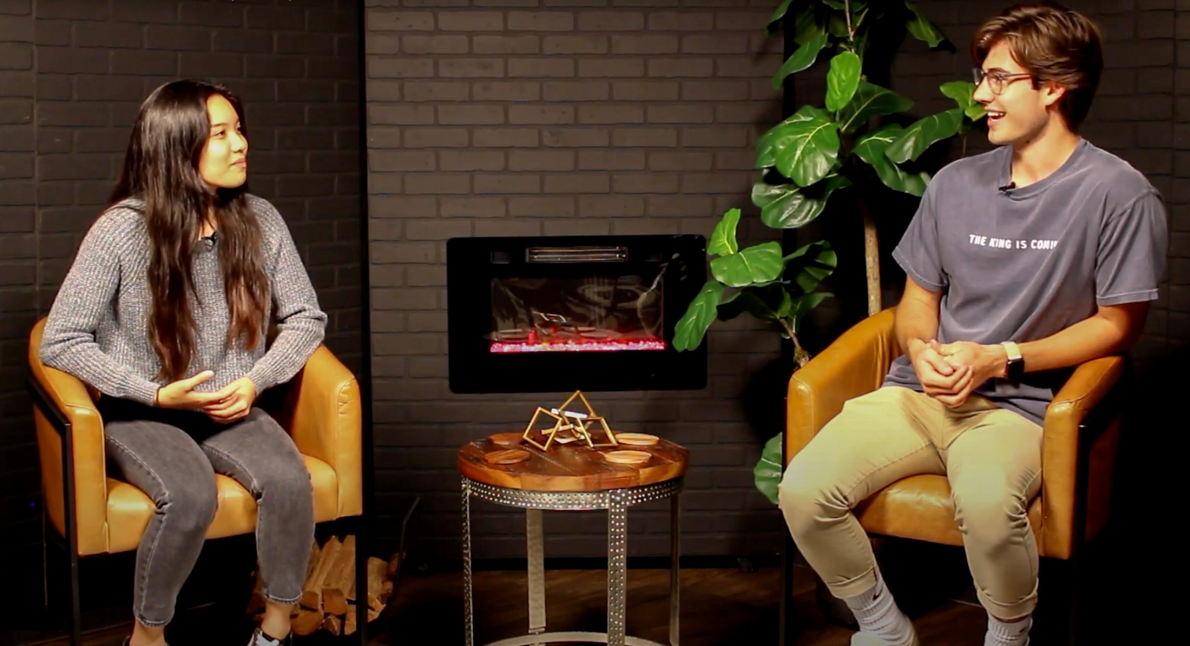 a young man and woman smiling and chatting together on a set of couches.