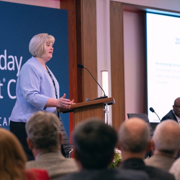 Smiling white woman speaking to a crowd from behind a podium.