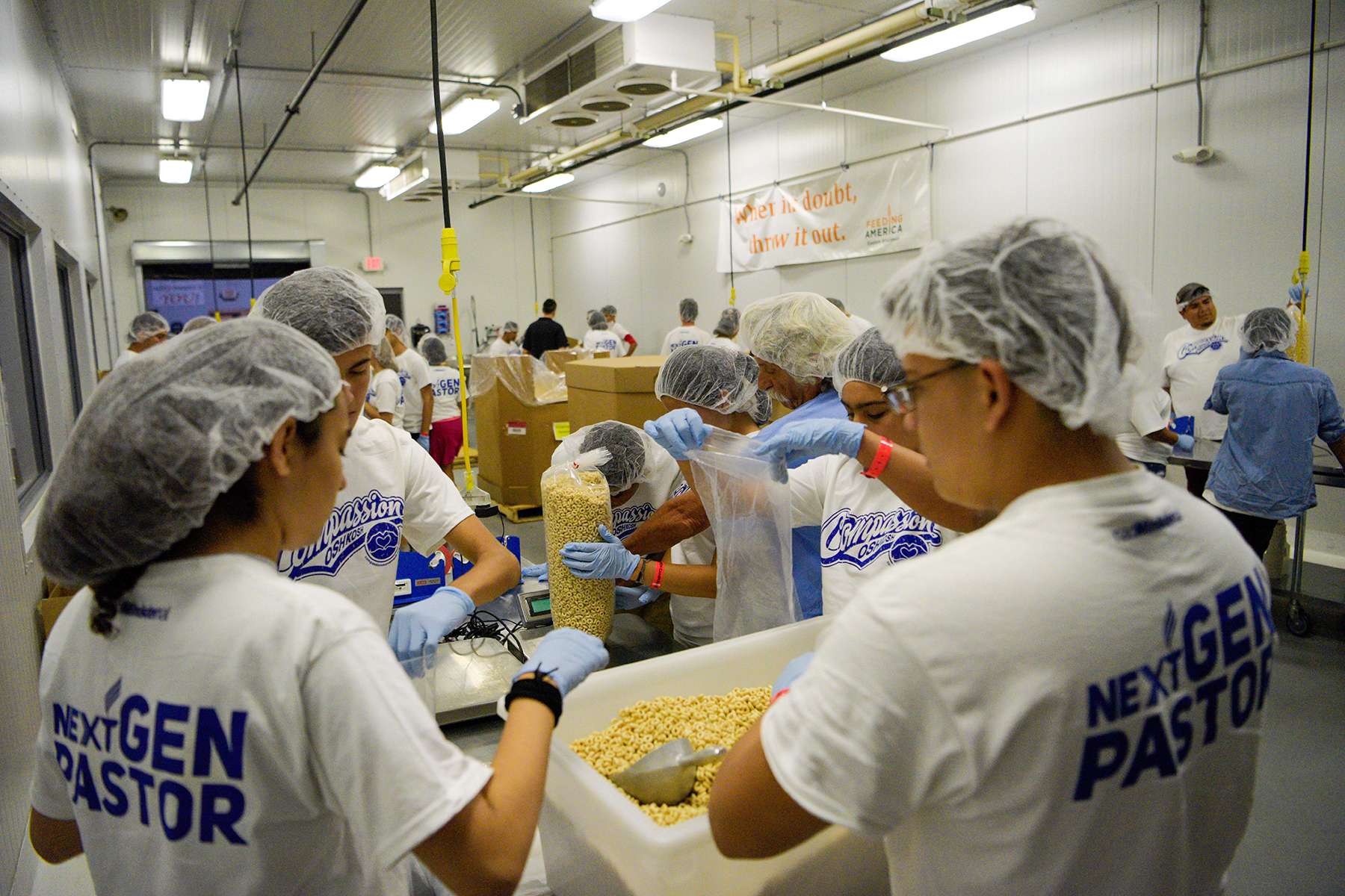young people wearing hair nets packing cereal into plastic bags.