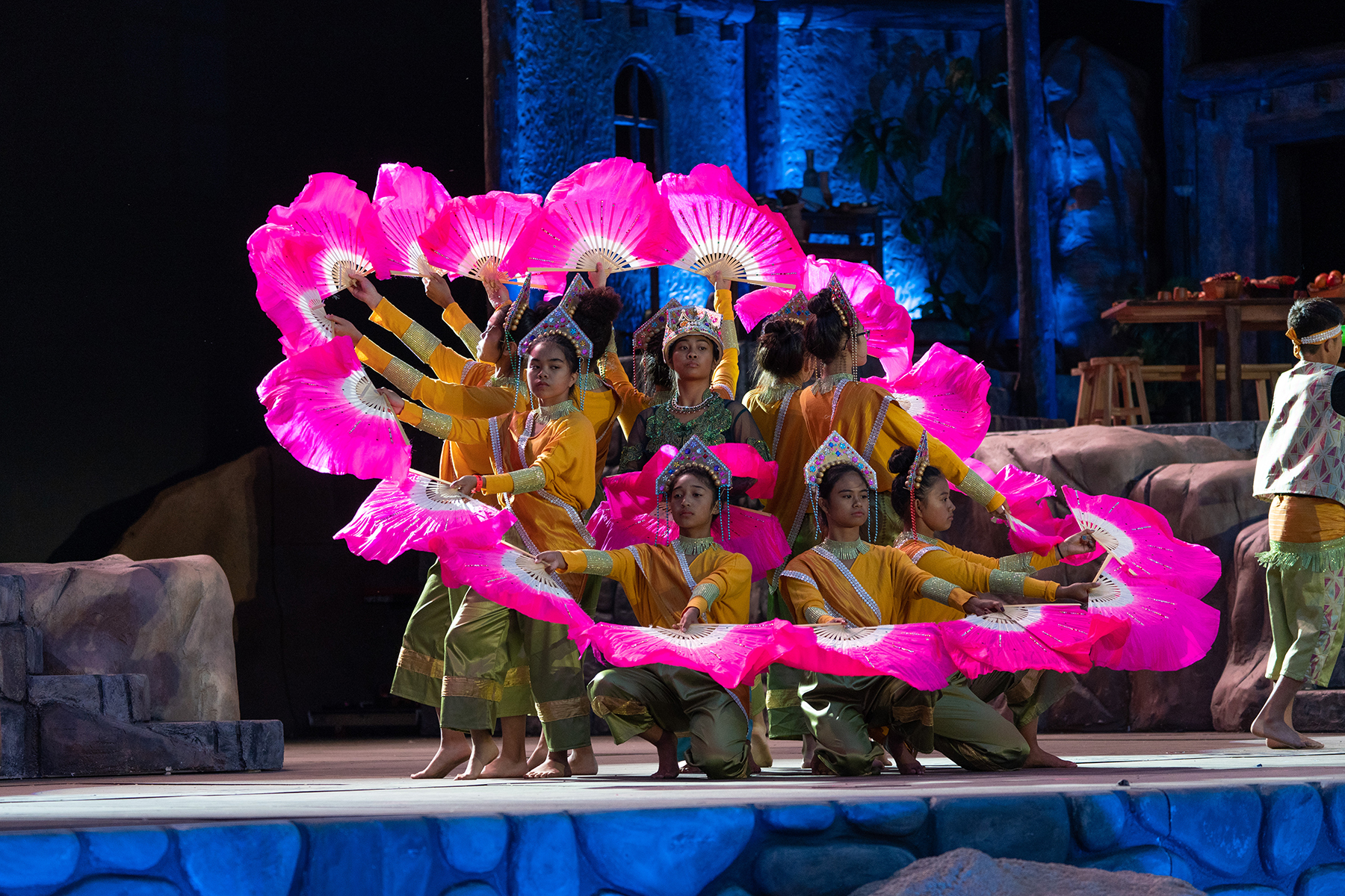Young Filipino women wearing a colourful cultural outfit and with pink fans on a stage.
