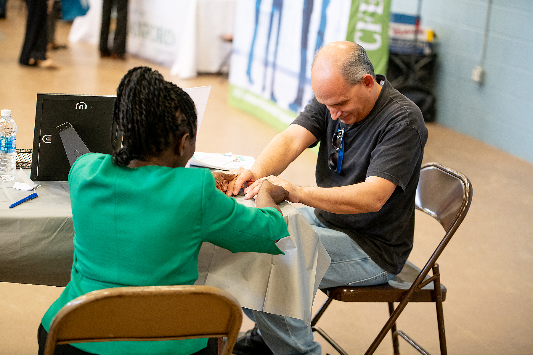 A black woman and white man seated at a table pray, holding hands. 