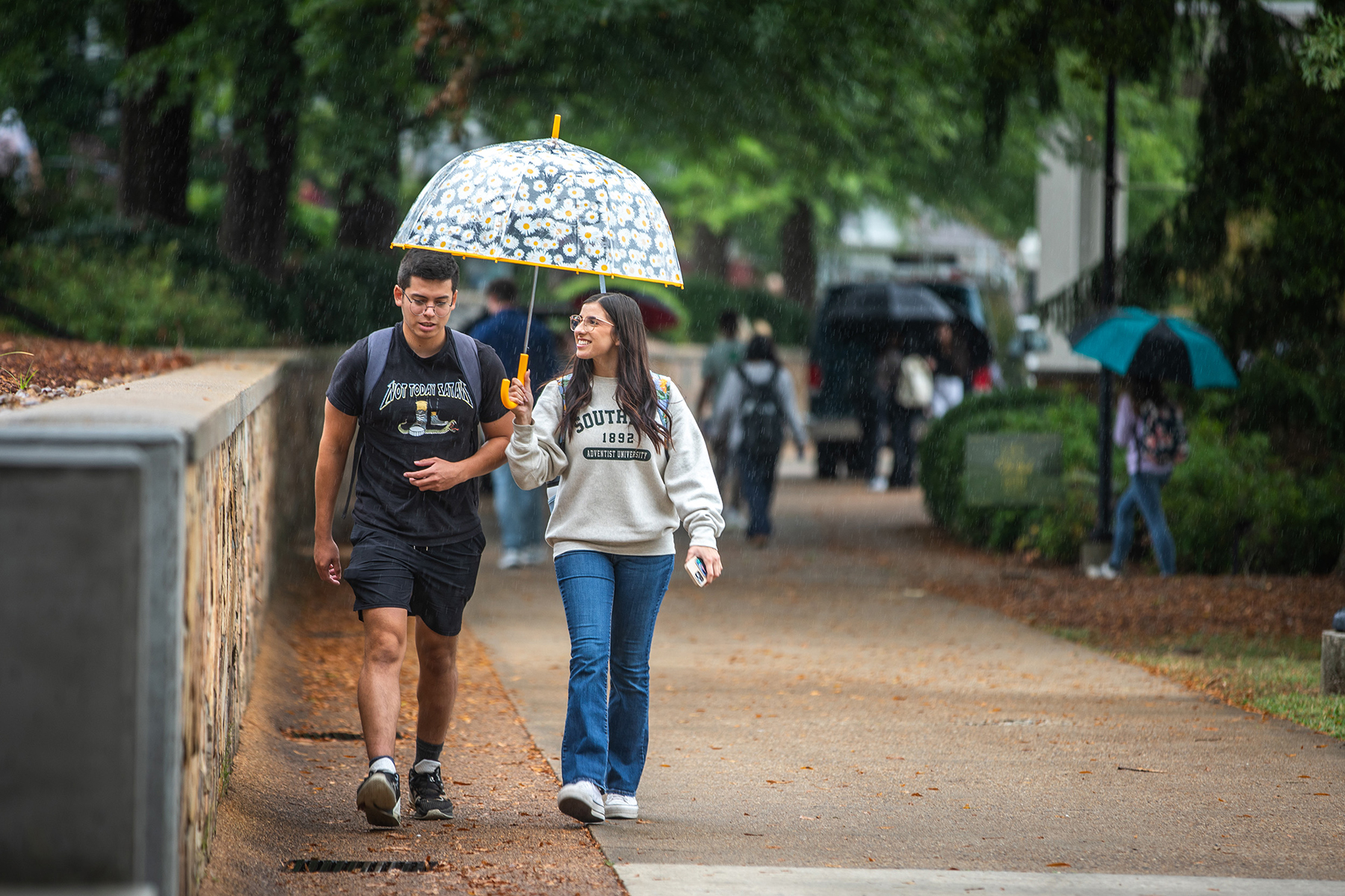 Young man and woman walking together on college campus under a flowered umbrella.