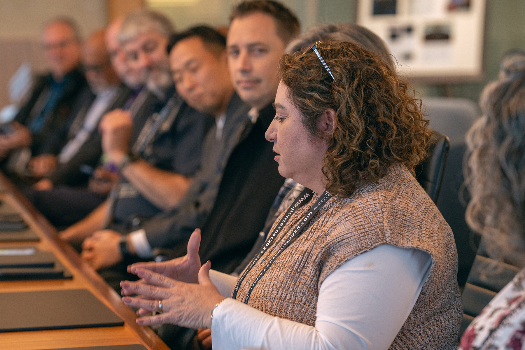 A woman speaks as men look on, all seated at a long table