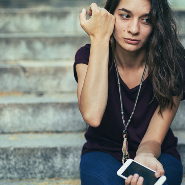 Young woman sitting on steps crying with cell phone in hand