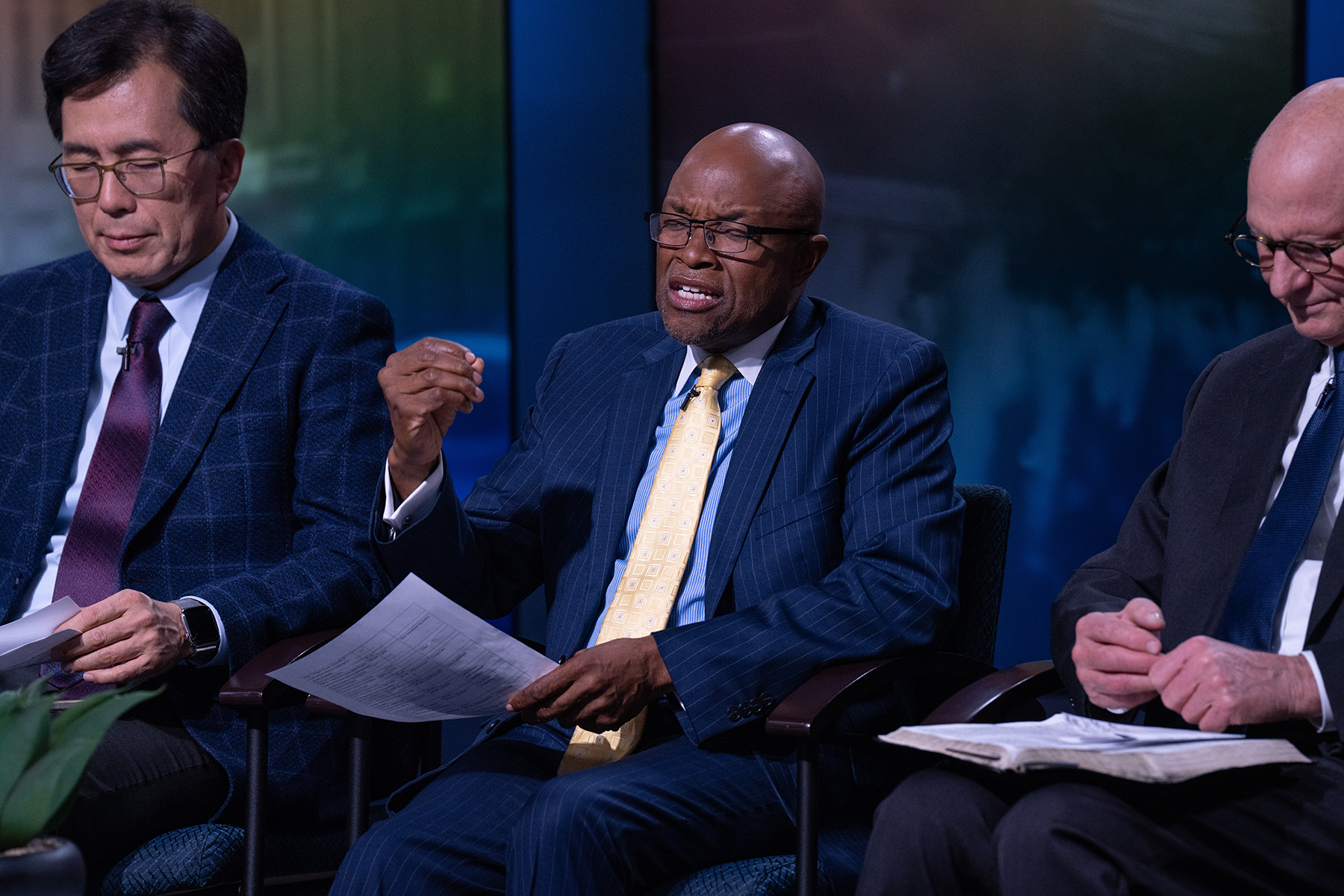 A diverse close-up shot of three men in suits; the one in the middle is praying.