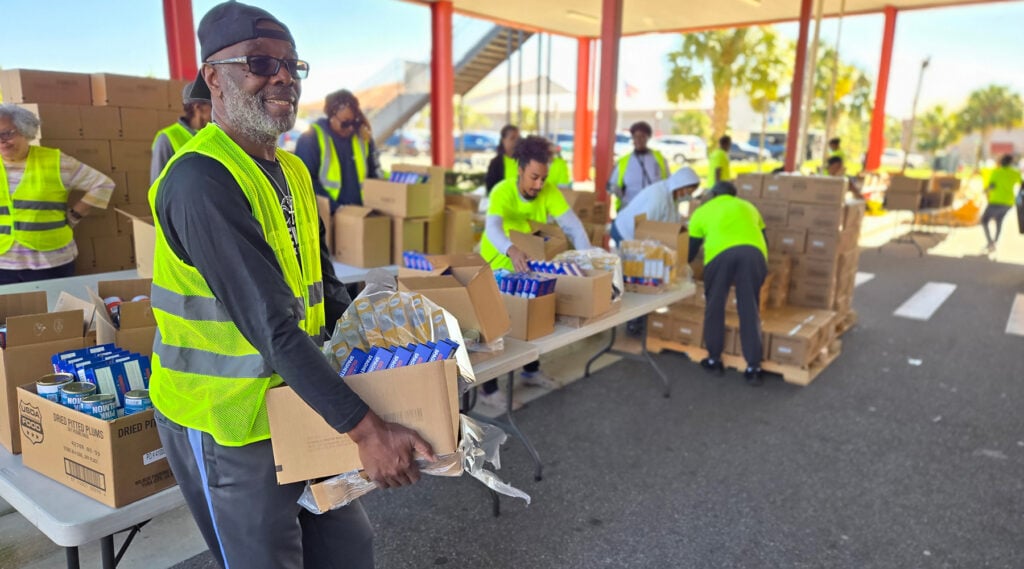 Black man wearing a yellow safety vest works at a food pantry