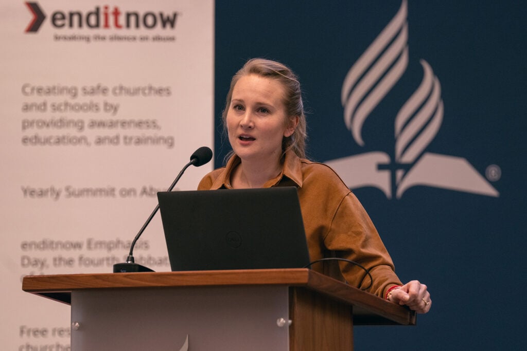 White woman speaks at a podium in front of an enditnow poster.