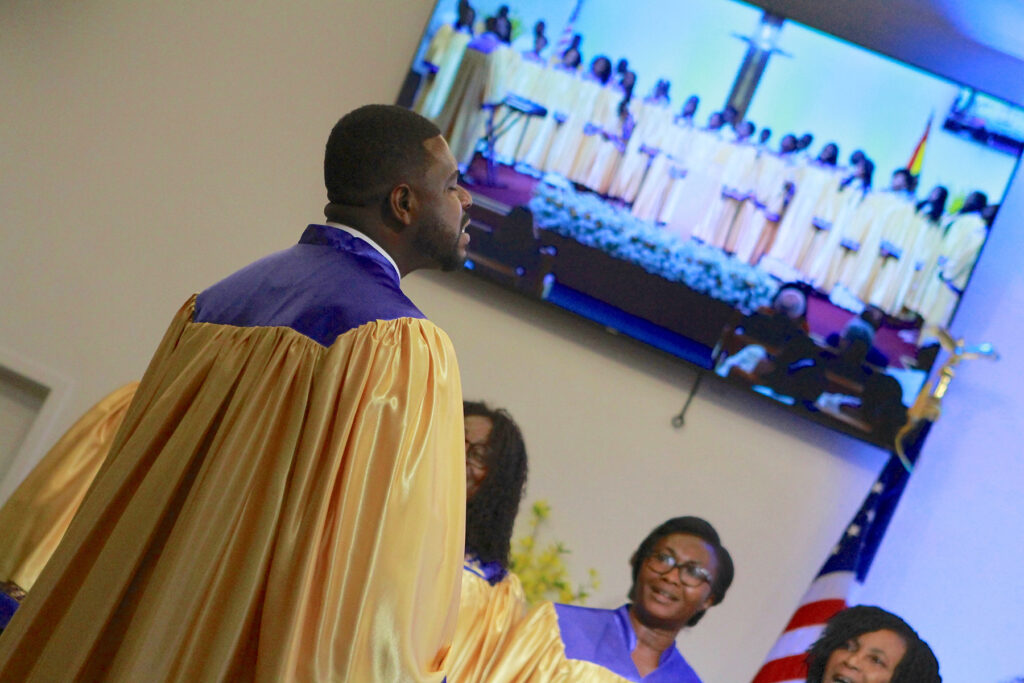 Close-up of Ghanaian choir in robes with image of full choir visible on a screen