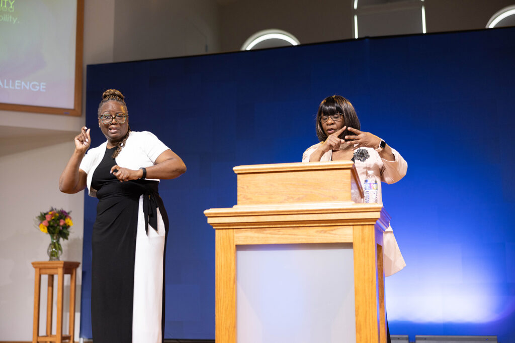 A woman interprets a presentation of another woman speaking behind a podium