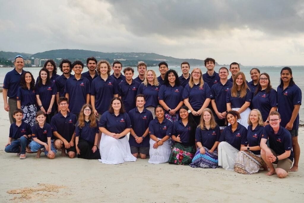 Large group of people posing on a beach in organized rows for a group photo.