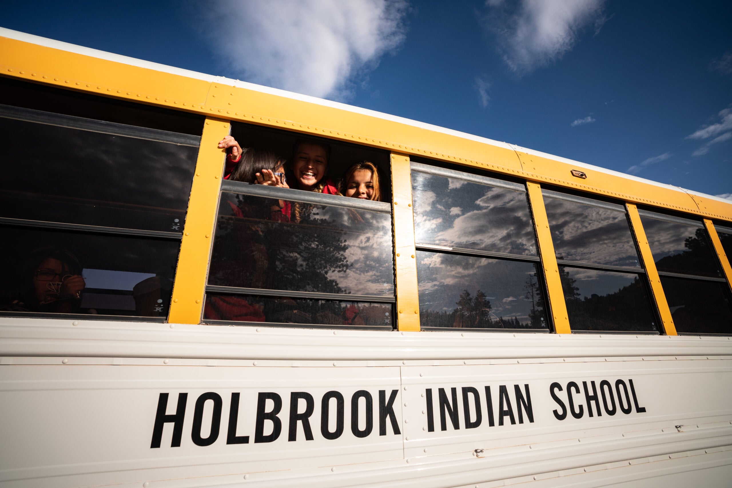 Students of Holbrook Indian School smile from the window of a school bus.