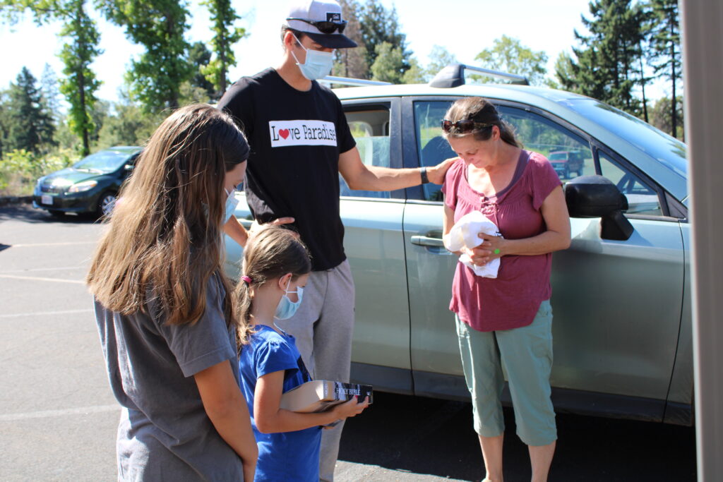 Pastor Garrison Chaffee prays with a grateful recipient of fresh food with Kyla and Rachel Moore. The food pick up was at the Paradise church parking lot. The church burned but serving others is still their priority.