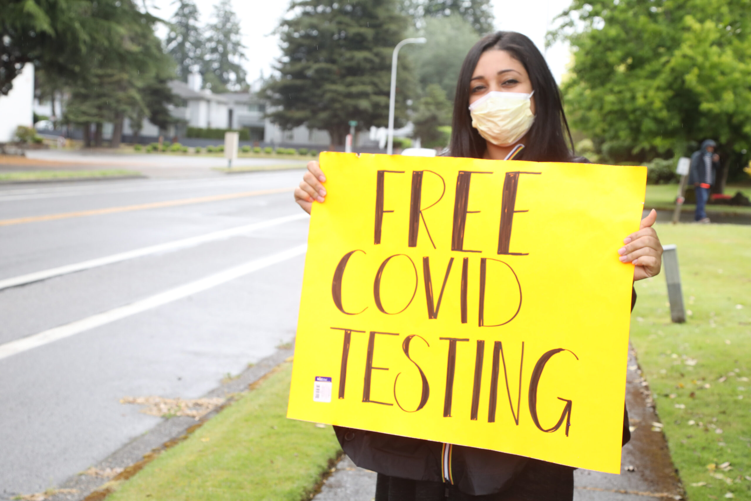 Jackie Langi holds a sign informing drivers about free COVID-19 testing and food boxes.