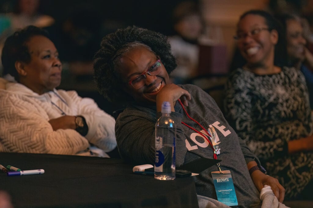 Three black women pictured laughting and smiling at a table.